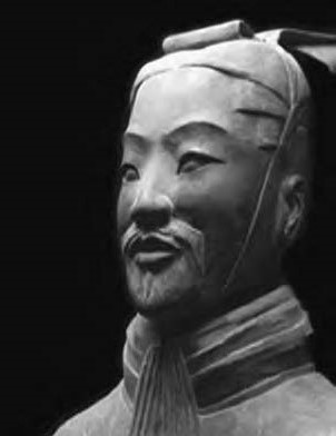 Black and white headshot photo of Sun Tzu, a legendary Chinese military strategist, depicted in a grey statue wearing a traditional scarf and headdress, with a thin mustache and goatee. His facial expression exudes a sense of wise pride and respect in his community. The image is lit from the top-left, symbolizing the enlightenment that comes from studying the ancient wisdom of Sun Tzu. Click to learn more about B2B sales strategies in the Protopian Grandmaster's Corner.